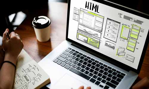 Eine Person macht sich Notizen in einem Notizbuch, während sie auf einen Laptop-Bildschirm blickt, auf dem Webdesign-Wireframes und Layout-Entwürfe mit hervorgehobenen Abschnitten für einen Onlineshop angezeigt werden.