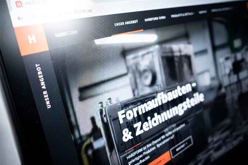 Computerbildschirm, auf dem eine Unternehmenswebsite in deutscher Sprache mit der Überschrift „Formaufbauten & Zeichnungsteile“ angezeigt wird. Das Layout umfasst ein für SEO optimiertes Navigationsmenü und ein unscharfes Hintergrundbild mit Industrie-Motiv.