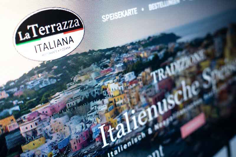 Auf einem Computerbildschirm ist die SEO-optimierte Website des Restaurants „La Terrazza Italiana“ zu sehen, auf der ein Bild einer Küstenstadt sowie ein deutscher Text über authentische italienische Gaumenfreuden zu sehen sind.