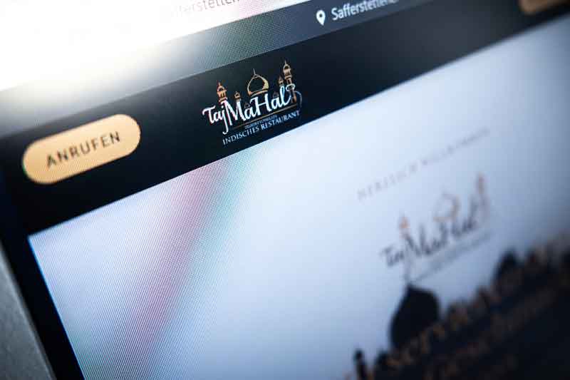 Nahaufnahme eines Computerbildschirms, auf dem die Website des „Taj Mahal Indisches Restaurant“ zu sehen ist, einem beliebten Restaurant in Passau, mit einer unscharfen Schaltfläche „Anrufen“ und dem Logo des Restaurants mit Kuppeln und Minaretten im oberen Bereich.